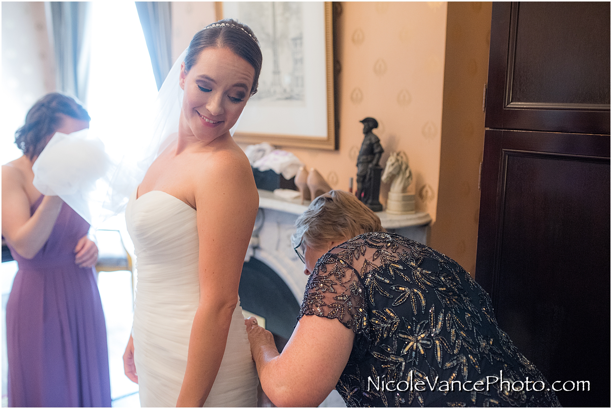 The bride's mom carefully fastens her buttons as she helps her daughter get ready.