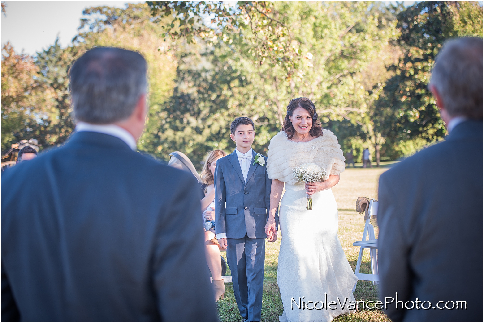 The bride walks down the aisle and smiles at her groom at Maymont Park.