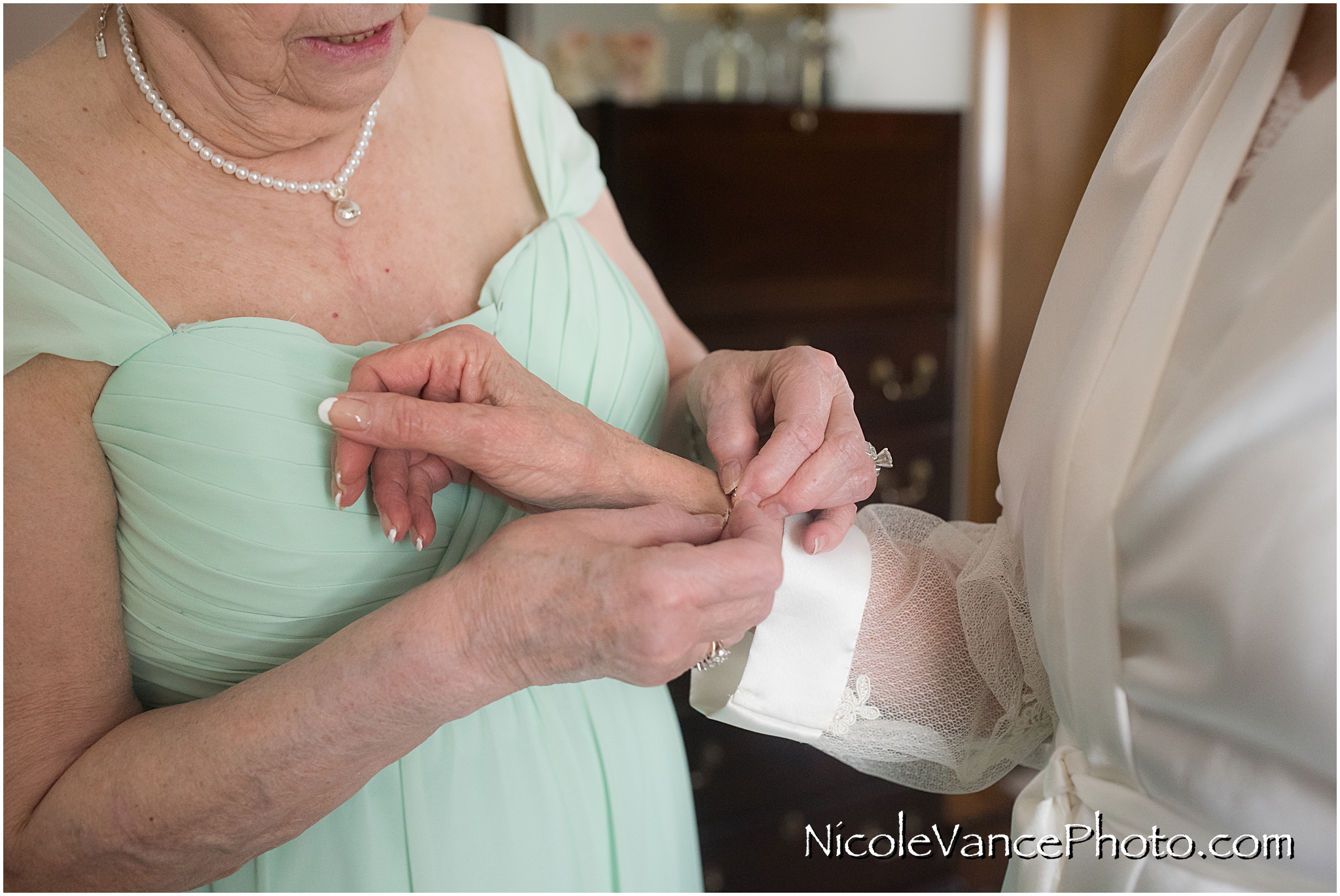 The bride's sister helps her put on her bracelet as she prepares for her wedding day.